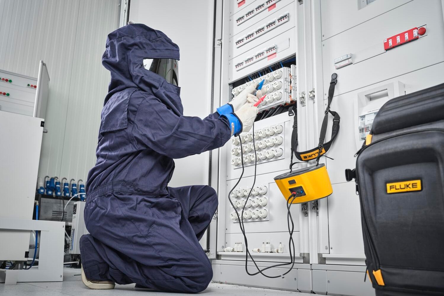 Technician in full personal protective gear taking measurements at an electrical panel