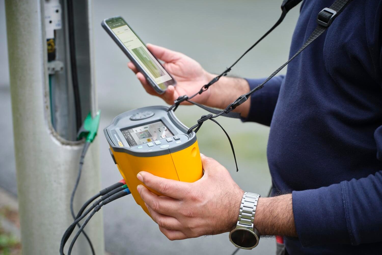 Mann, der einen Installationstester in der einen Hand und sein Smartphone in der anderen Hand hält, um die Ergebnisse abzulesen