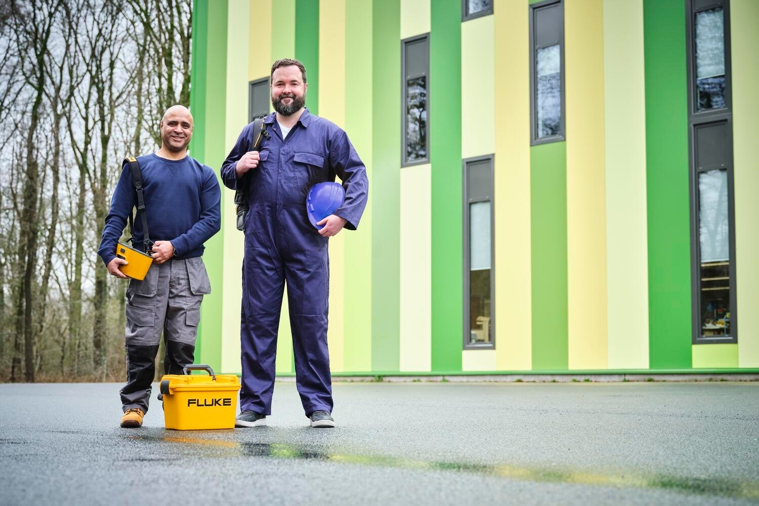 Dos técnicos en el exterior de un colorido edificio, listos para trabajar con sus instrumentos Fluke