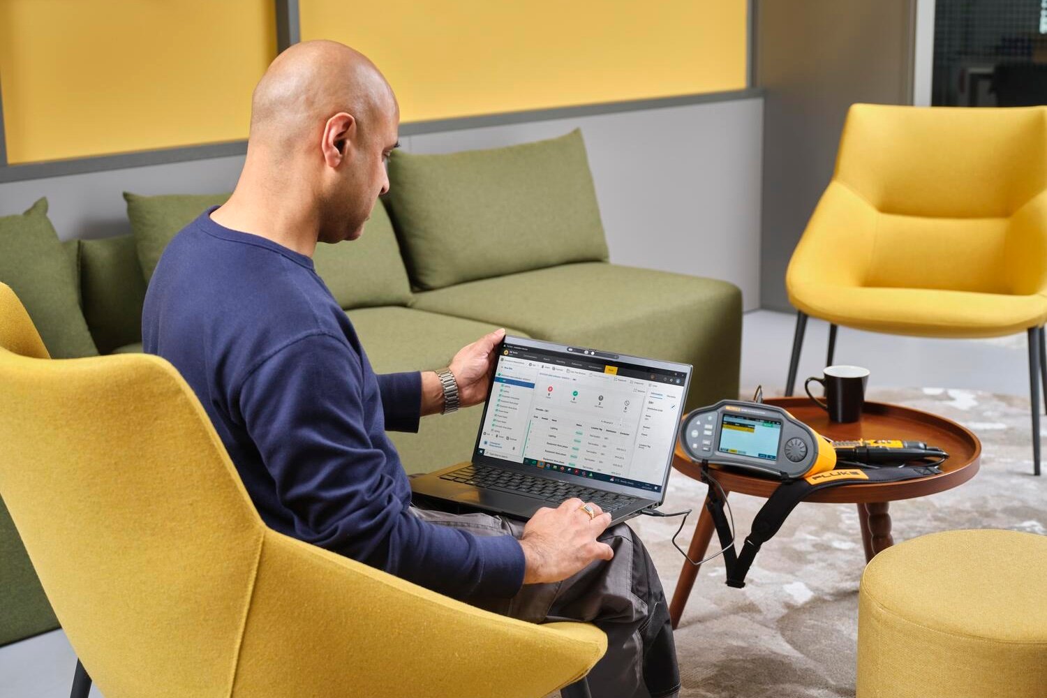 Homme avec un ordinateur portable sur ses genoux, travaillant avec le logiciel TruTest et un testeur d´installation Fluke