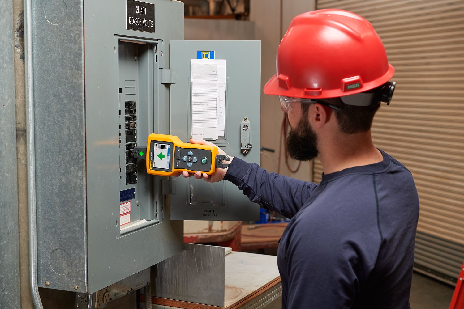 Man wearing a red hard hat uses a wire tracer to take a measurement in a breaker box