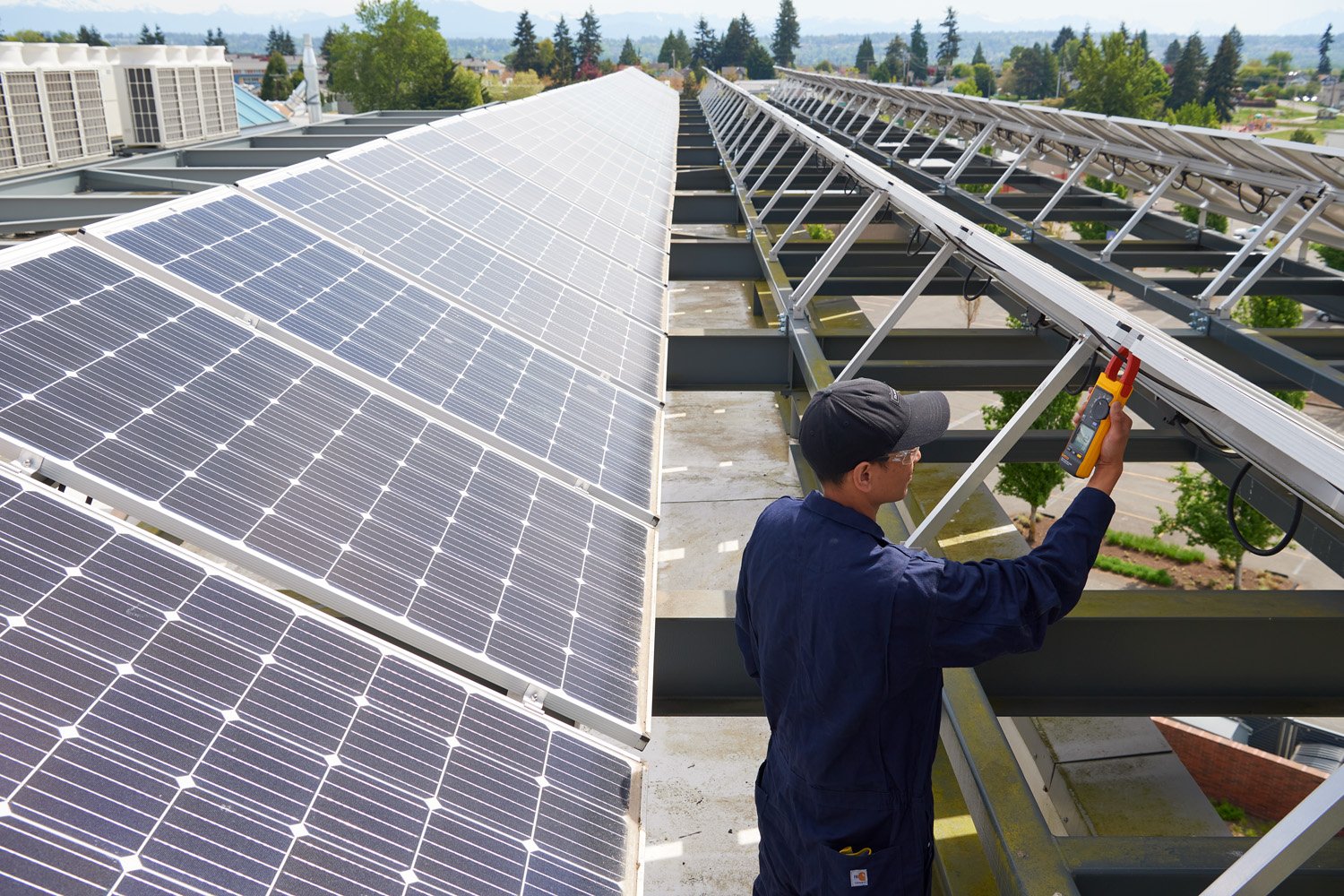 A technician standing between rows of solar panels, taking readings at the rear of one panel with a Fluke 393 FC.