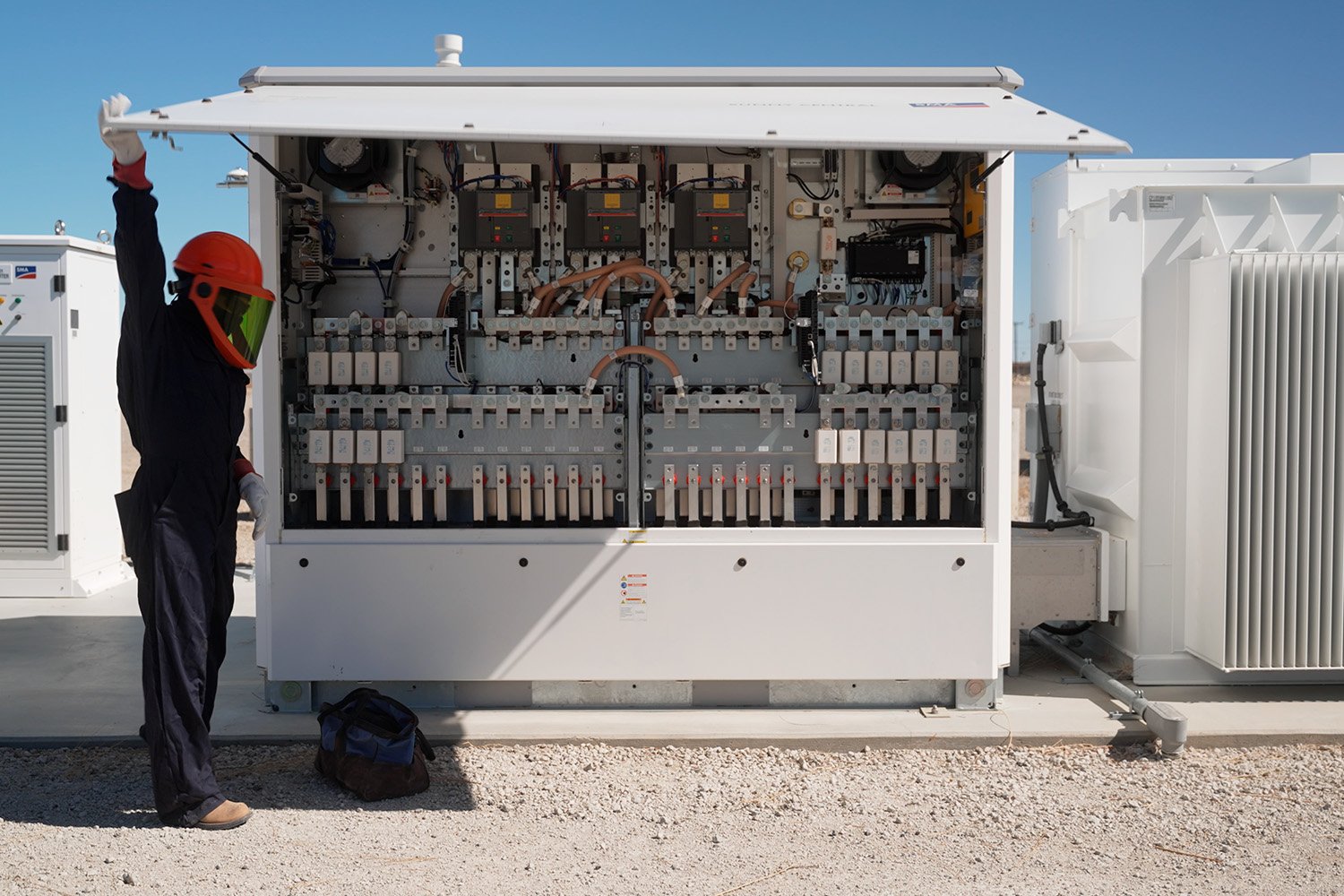 Electrician in protective equipment opening an inverter cabinet at a solar array