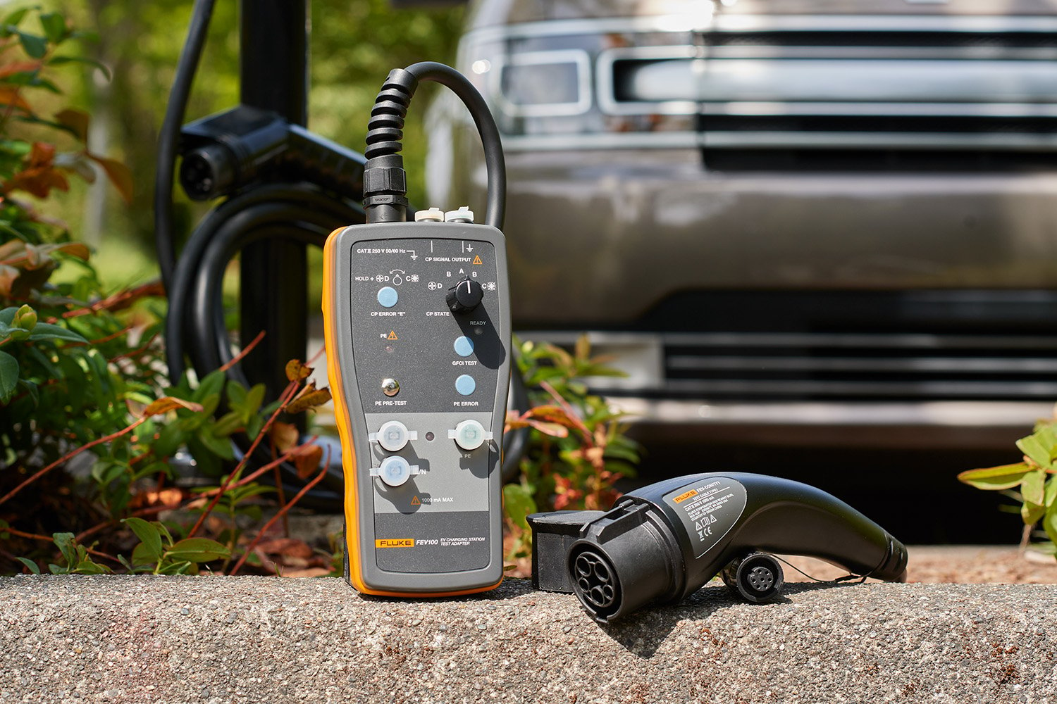 Fluke FEV100 and connector sitting on a curb in front of an electric vehicle at a charging station