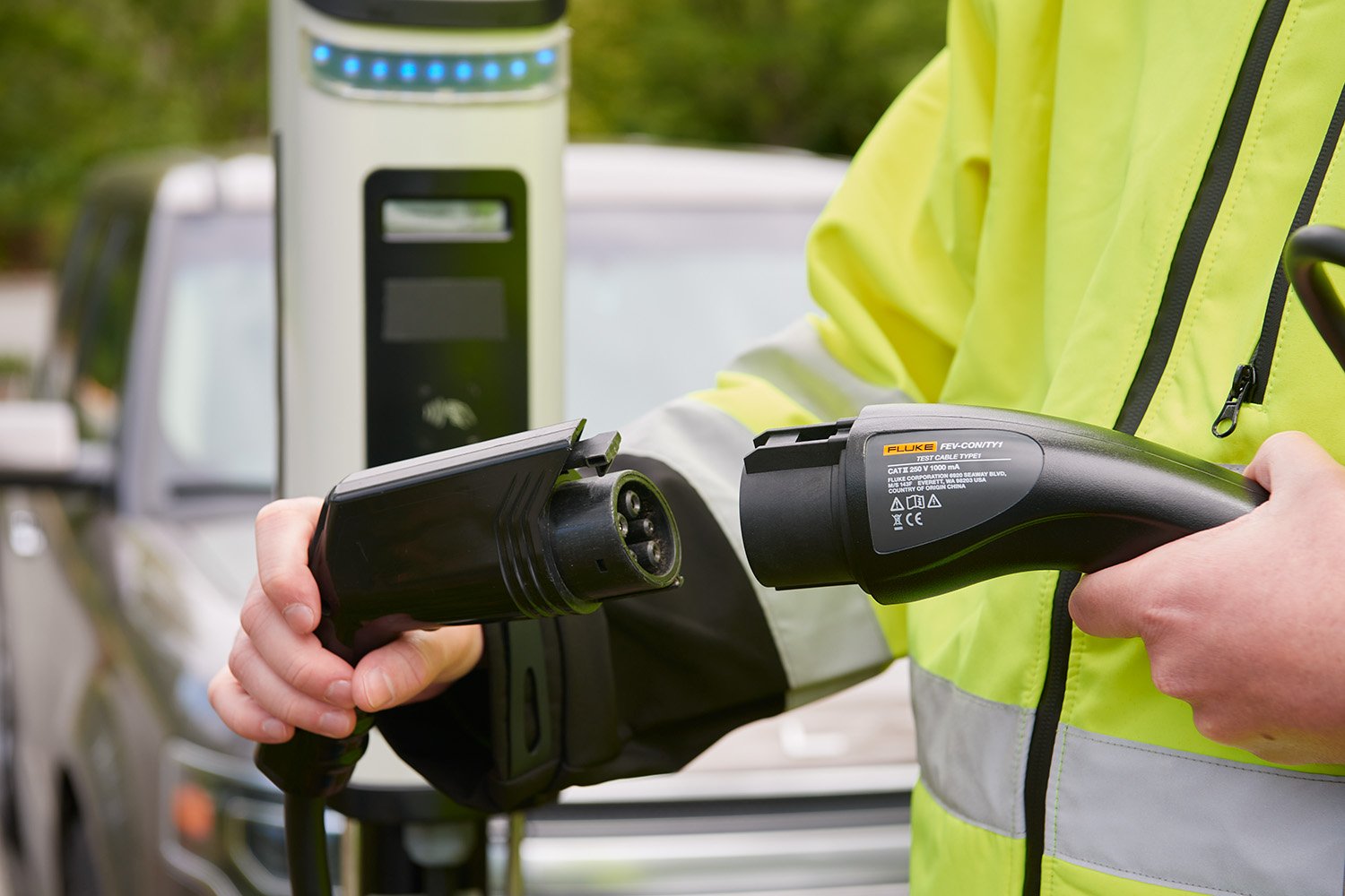 Man in optic yellow jacket connecting the Fluke adapter to the cable on an EV charging station