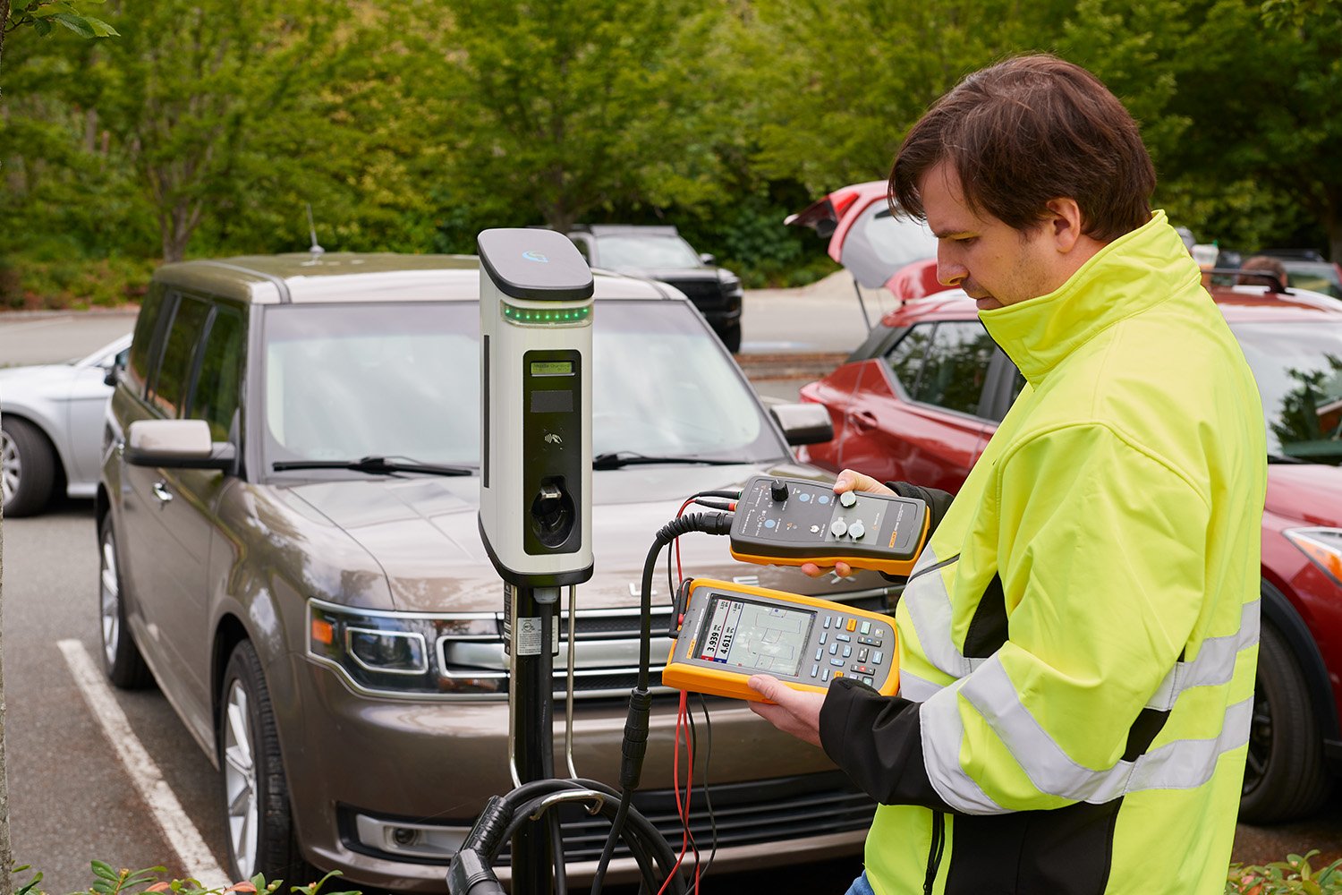 Man in optic yellow jacket testing an EV charging station with an FEV100 and a Fluke scopemeter