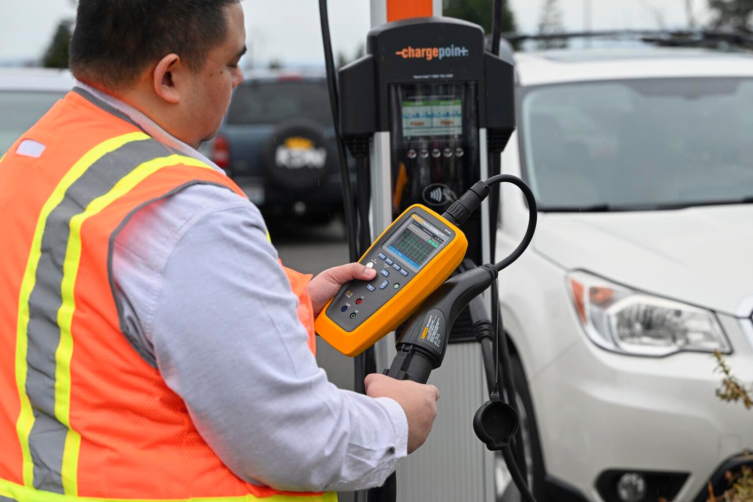 Technician in an orange vest testing an EV charging station with a Fluke FEV150 EV Charging Station Analyzer
