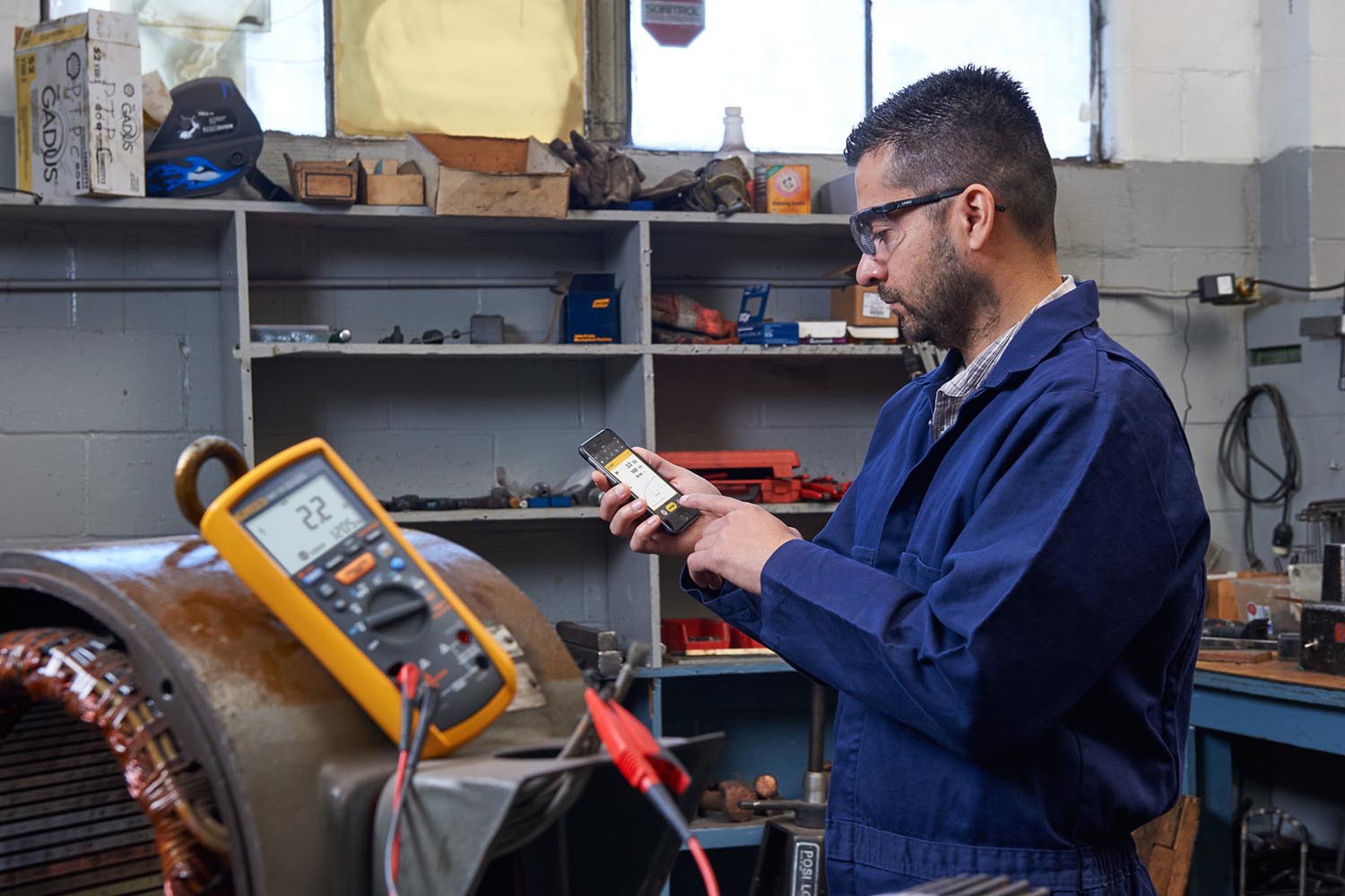 A technician in a shop makes measurements on an industrial motor and views results on his smartphone