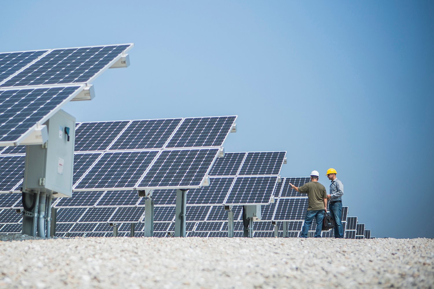 图片：两个头戴安全帽的人正站在一排太阳能电池板的末端