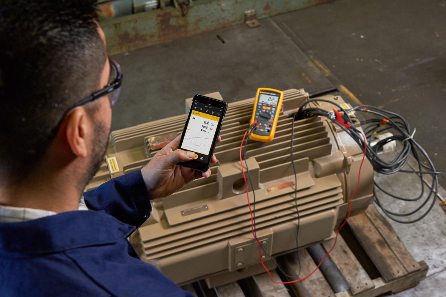 A technician in a shop makes measurements on an industrial motor while watching the results on his smartphone