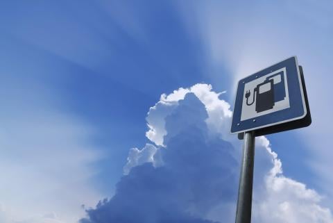 EV charging station sign against a bright blue sky with fluffy clouds