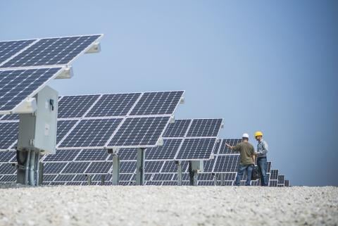 Obrázek techniků s přilbami stojících na konci řady solárních panelů