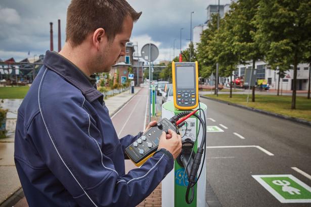 Man in optic yellow jacket testing an EV charging station with an FEV300 and a Fluke scopemeter